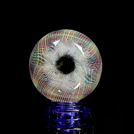 A multicolored glass marble with a mix of vibrant and muted tones, featuring a patterned design. The marble appears to have a convex surface.