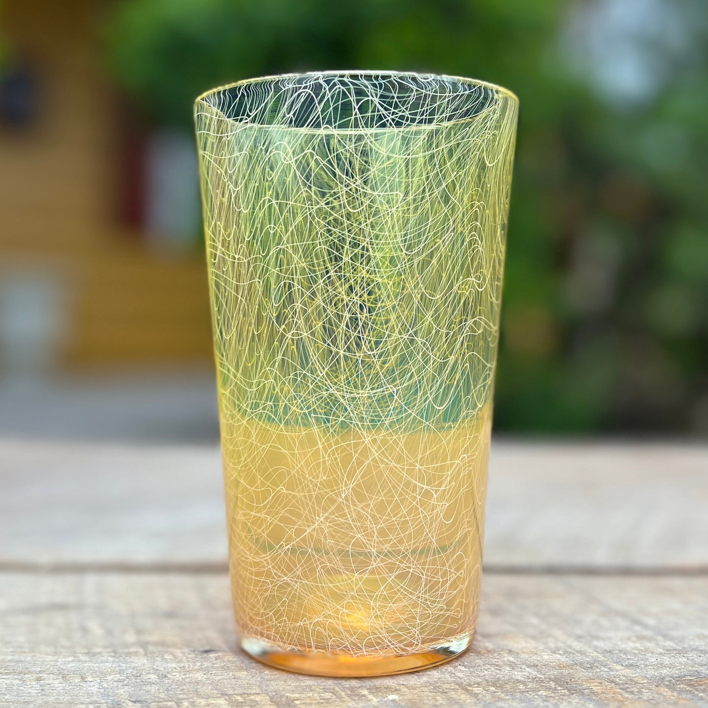 A cylindrical handcrafted glass with yellow hues and white scribbles.