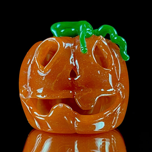 A glass pendant necklace with a orange and green pumpkin-shaped figure on a yellow cord.