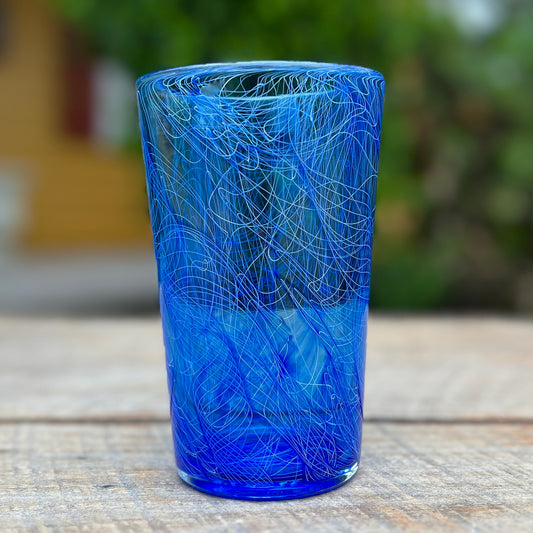 A cylindrical, blue glass pint with a swirling pattern, crafted from glassblowing.