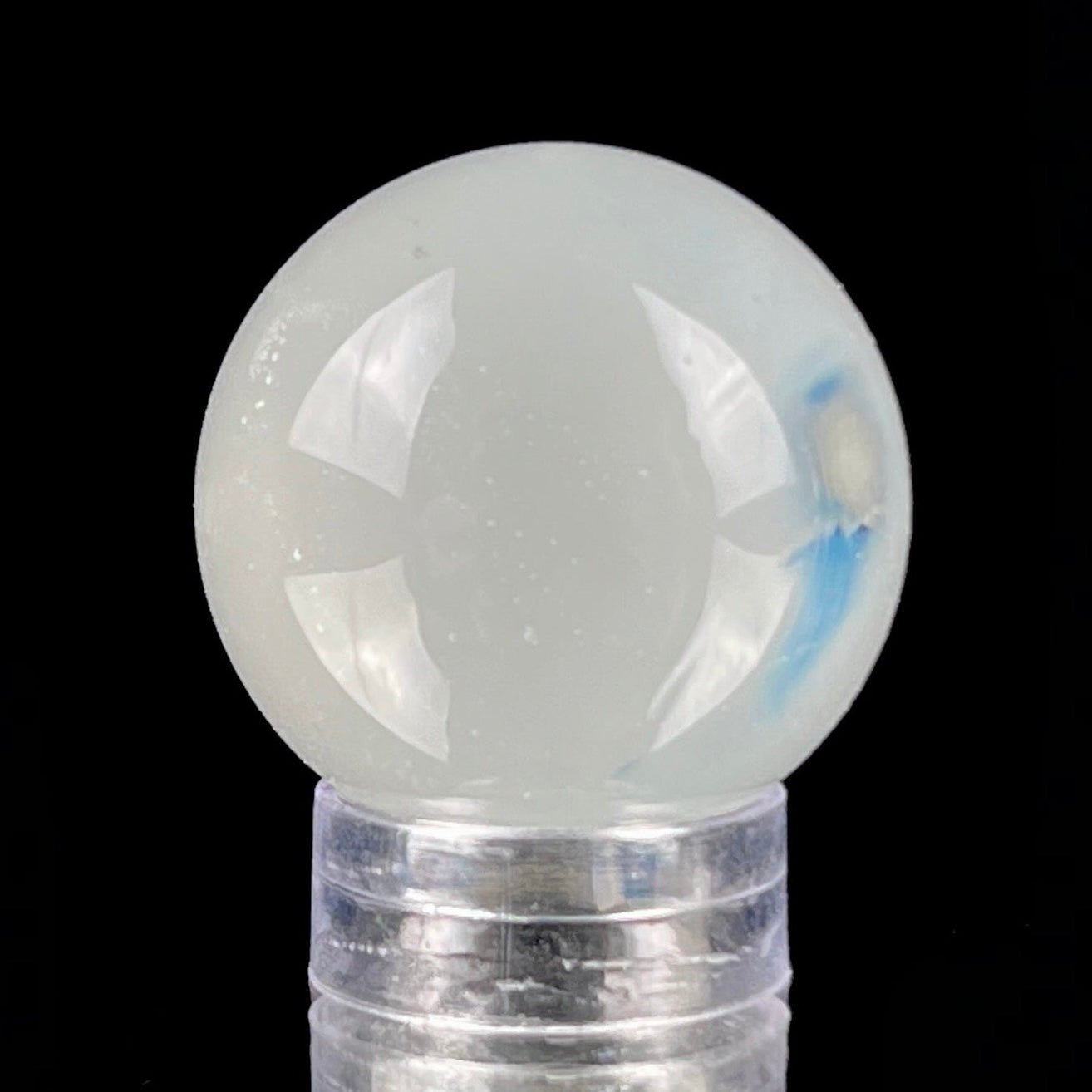 A glass marble with a design of blue dots on a white background, approximately 26mm in diameter, displayed on a clear stand.