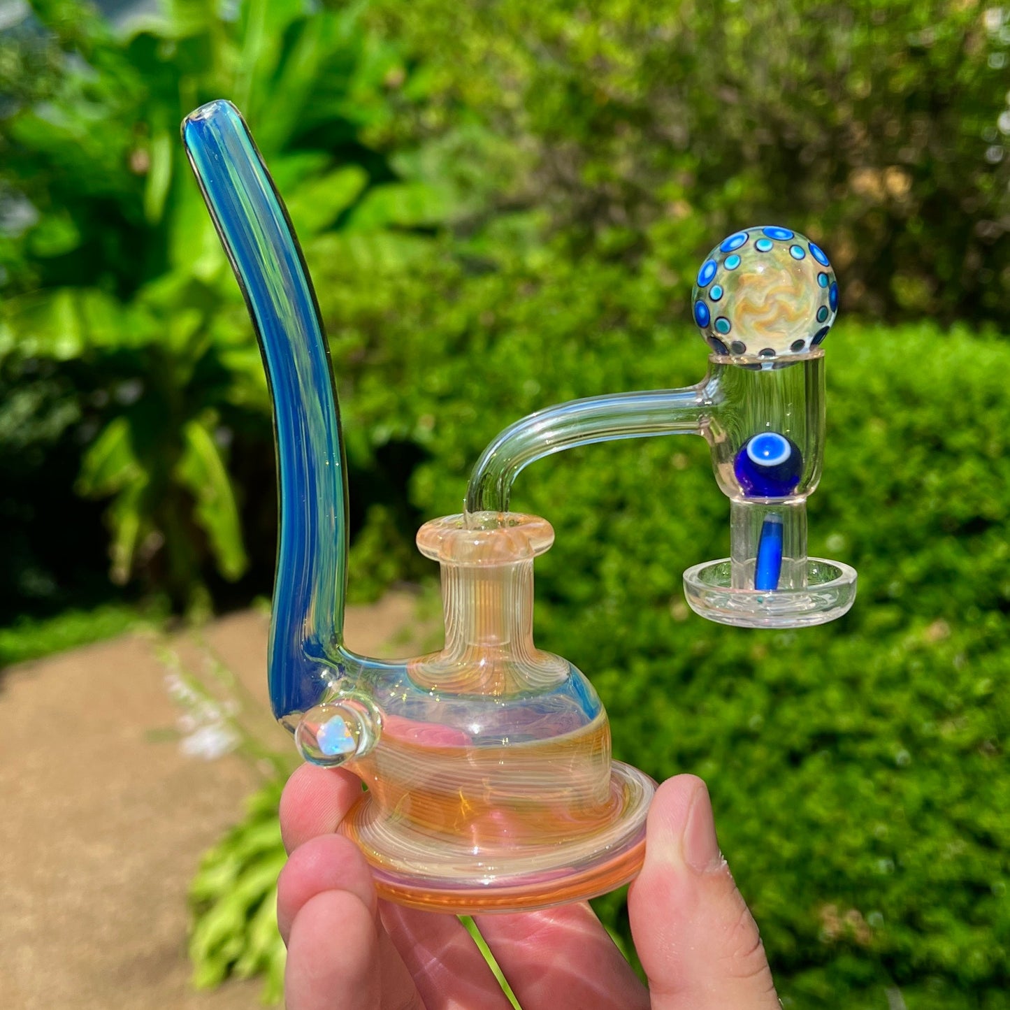 Glass smoking device held in a hand with a blurred green outdoor background