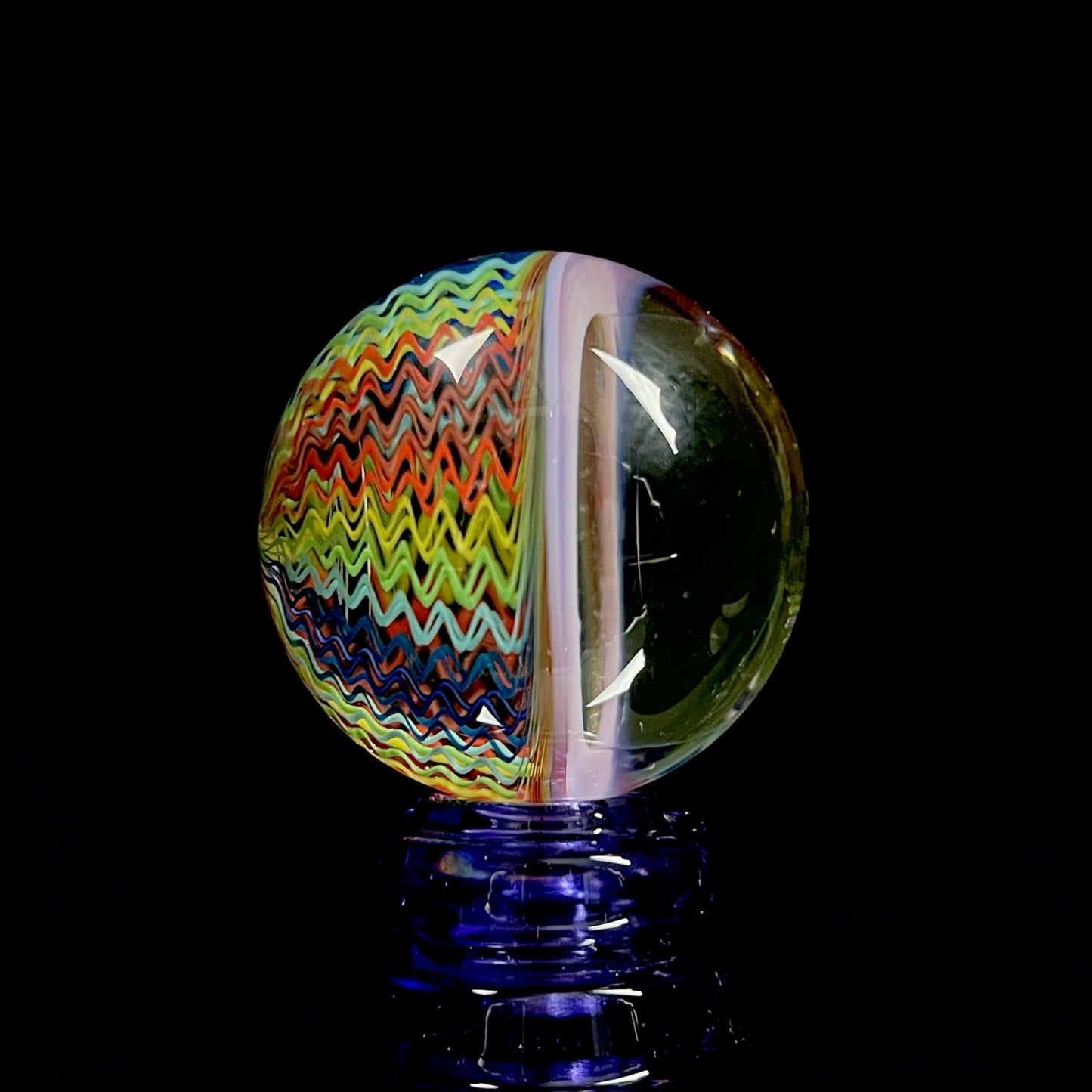 A multicolored spiral pattern marble with a predominantly black center and radiating swirls of blue, red, and green.