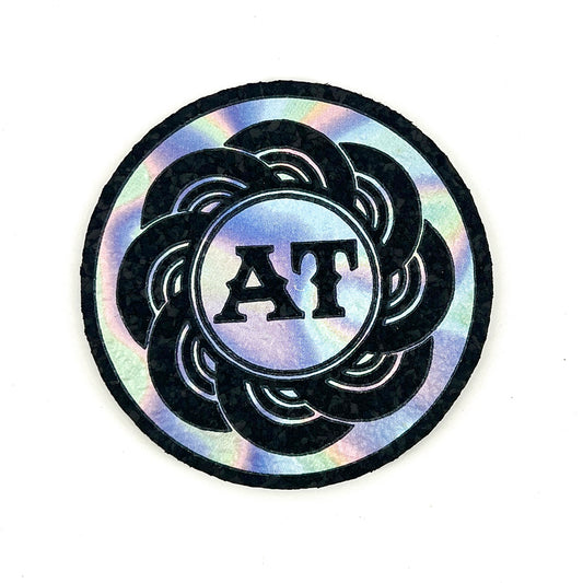 Holographic circular mat with 'AT' initials on a white background.