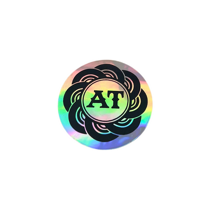 Holographic sticker with 'AT' initials on a white background.