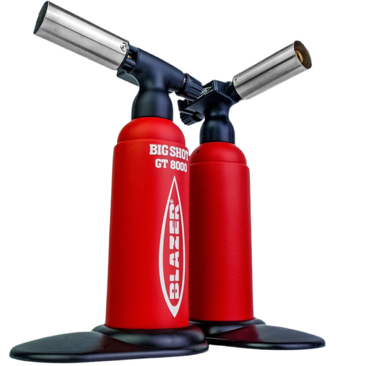 Two Blazer Big Shot butane torches in red color with glow-in-the-dark labels, positioned upright with a black base.