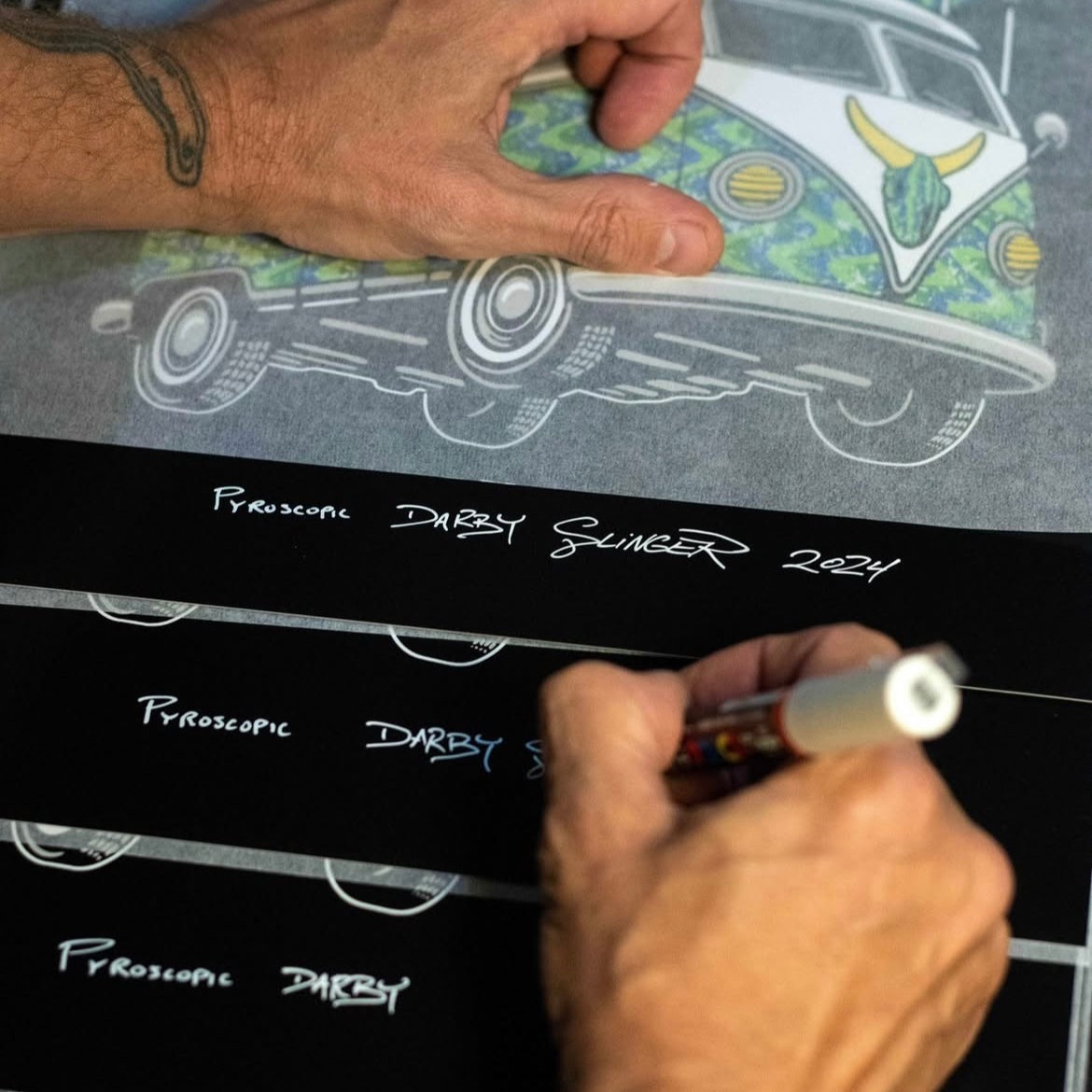 Person signing a print of a car illustration with a pen.