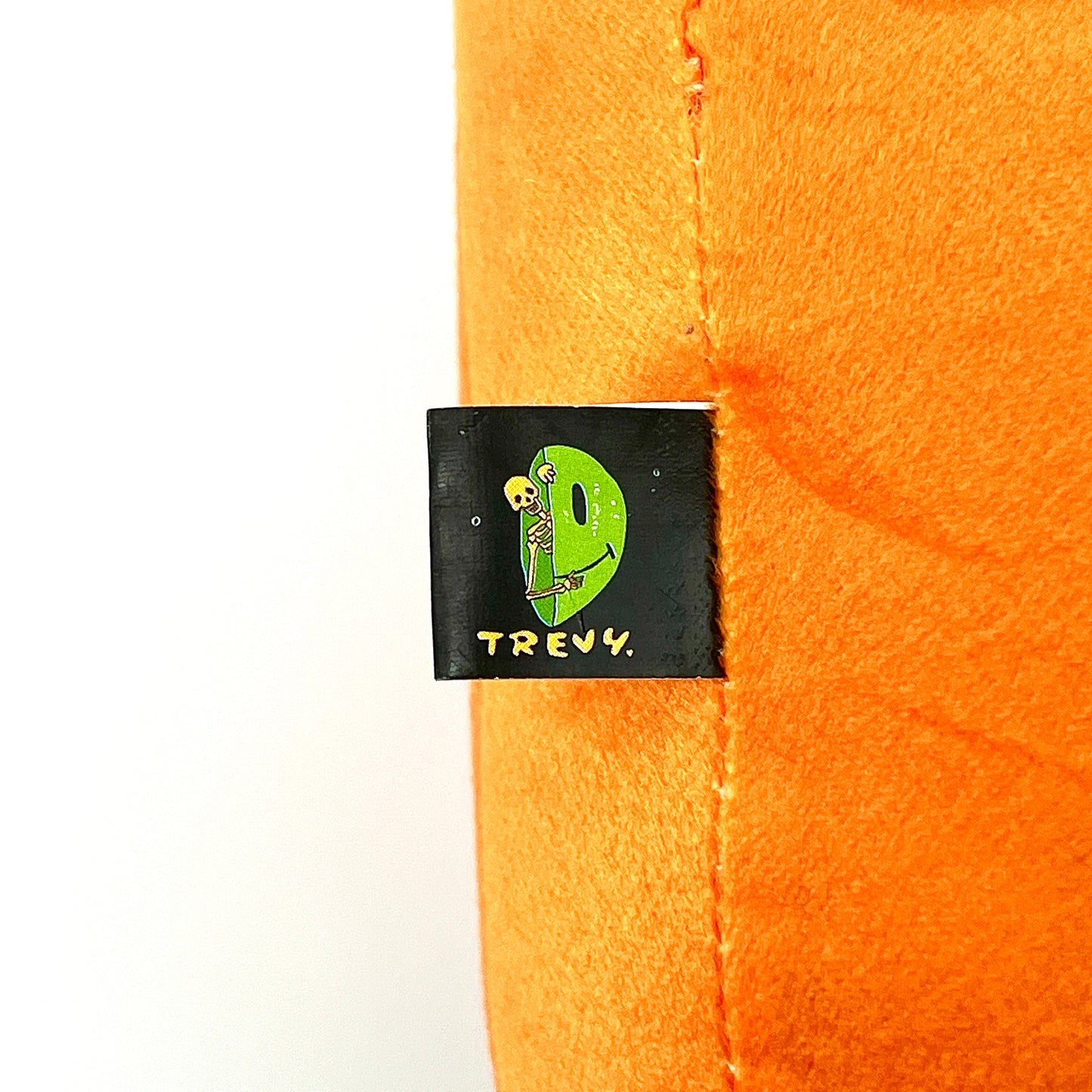 A plush toy designed by Trevy Metal featuring a skeleton peeking out from an orange shell, resembling a pumpkin.
