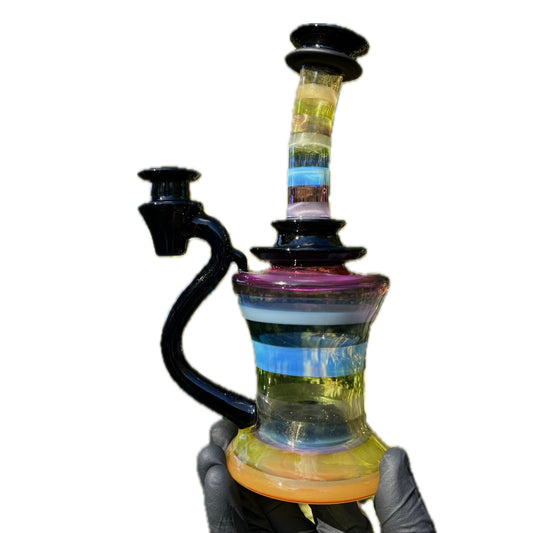 A multicolored glass piece with a 6-hole puck perc and encalmos, held in a gloved hand.