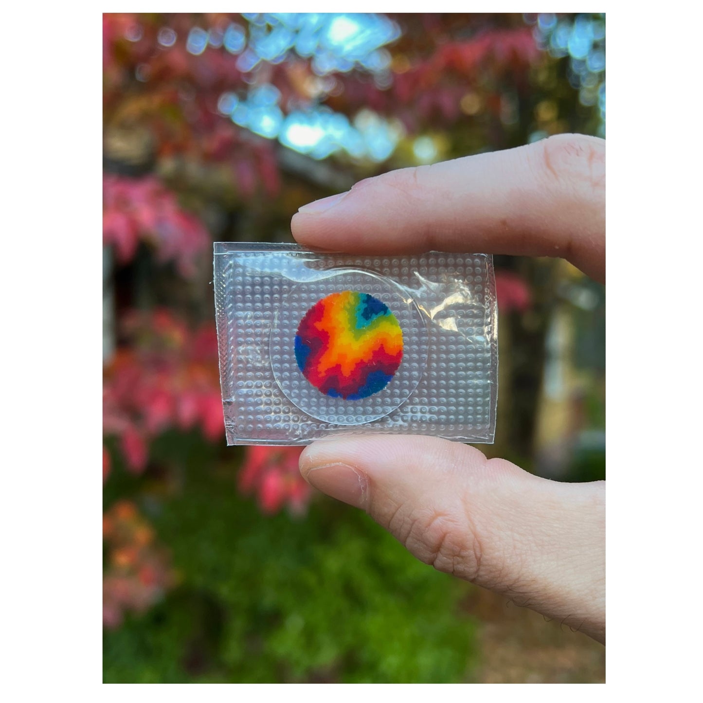 Hand holding a clear package with a tie-dye object against a blurred natural background.