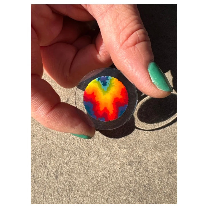 Hand holding a round object with a colorful pattern on a neutral background.