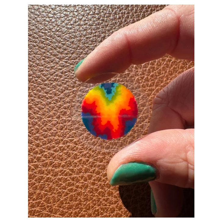 Hand holding a small tie-dye glass coin on a brown leather surface.