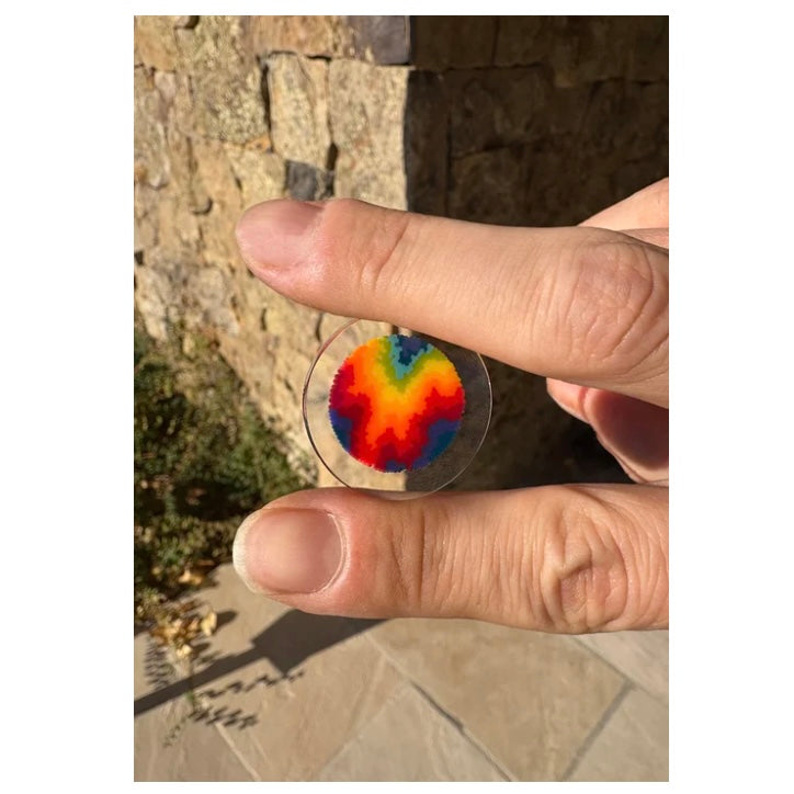 Hand holding a transparent disc with a colorful pattern against a stone wall background.