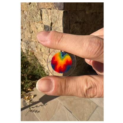 Hand holding a transparent disc with a colorful pattern against a stone wall background.