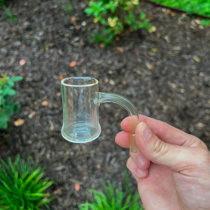 Hand holding a small clear quartz bucket against a natural background with greenery.