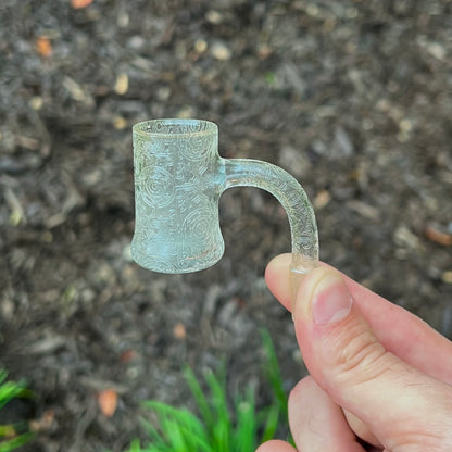 Sandblasted quartz bucket with intricate design held by a hand against a natural background.