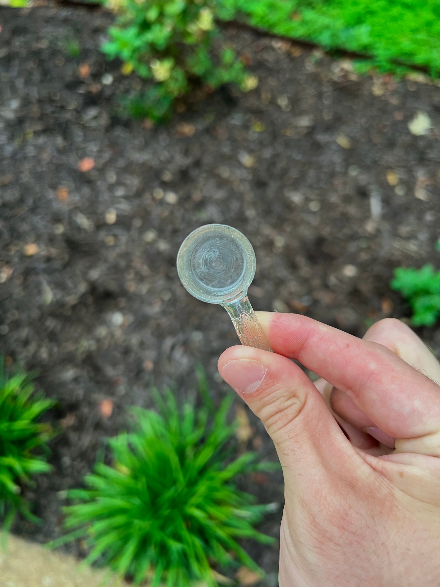 Hand holding a small quartz bucket against a garden background.