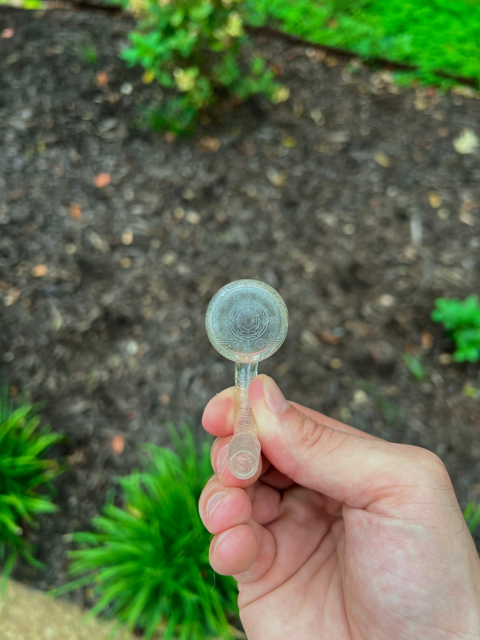 Hand holding a small transparent object with a textured surface against a blurred natural background