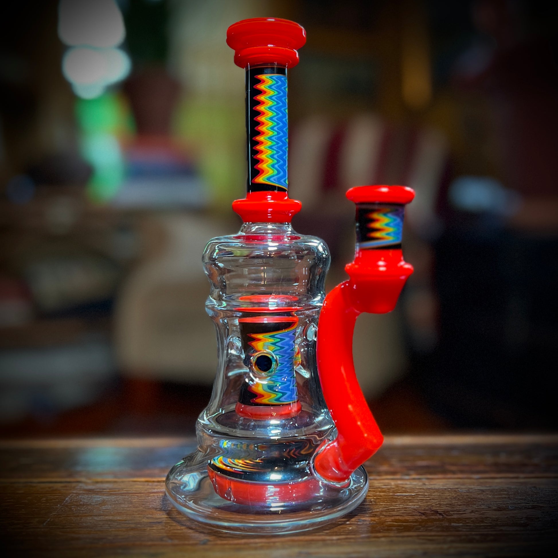 A multicolored glass piece with red accents and rainbow line work, featuring a 9-slit perc and a 14mm joint.