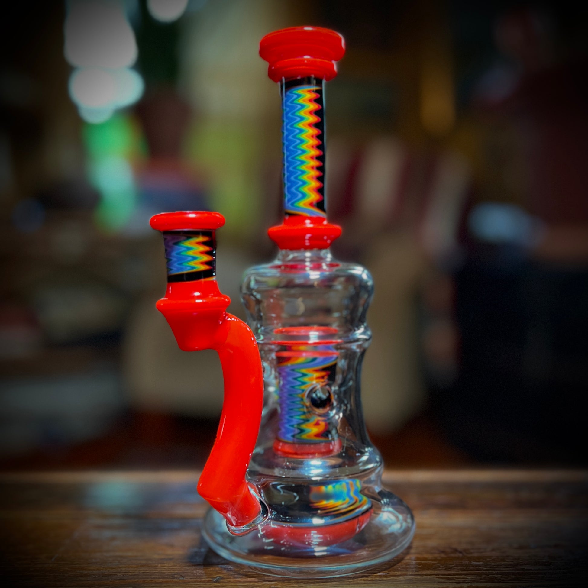 A multicolored glass piece with red accents and rainbow line work, featuring a 9-slit perc and a 14mm joint.