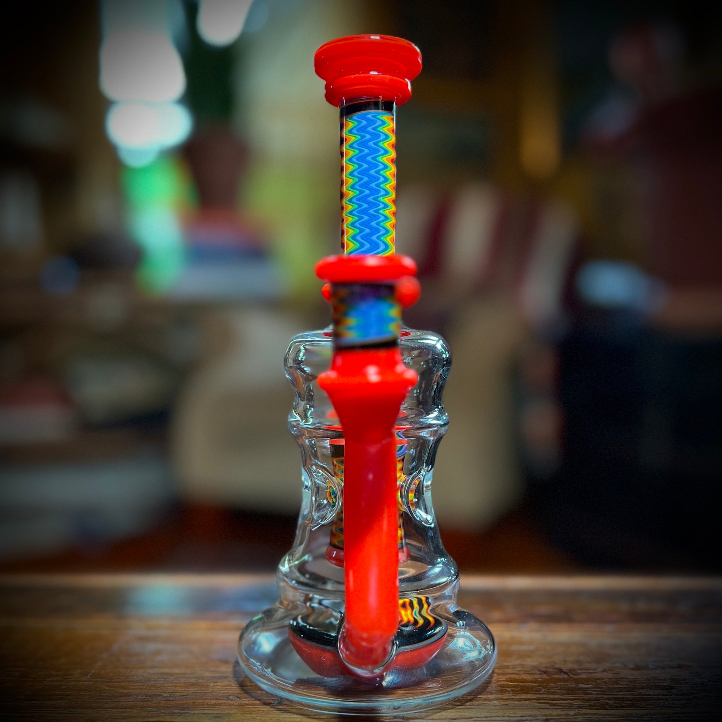 A multicolored glass piece with red accents and rainbow line work, featuring a 9-slit perc and a 14mm joint.