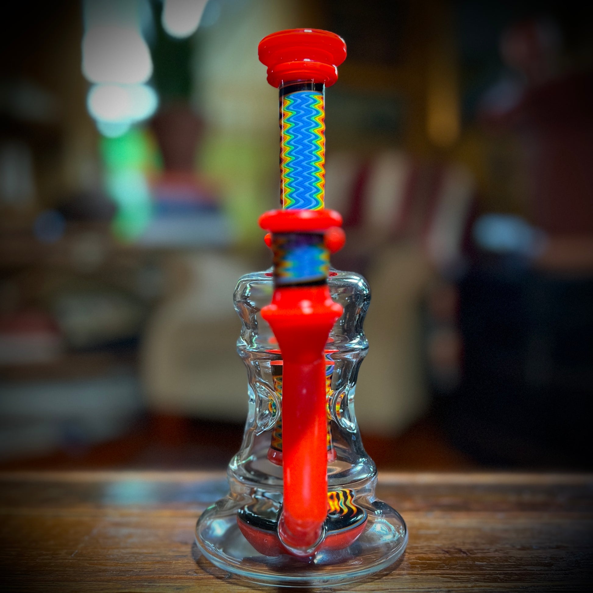 A multicolored glass piece with red accents and rainbow line work, featuring a 9-slit perc and a 14mm joint.