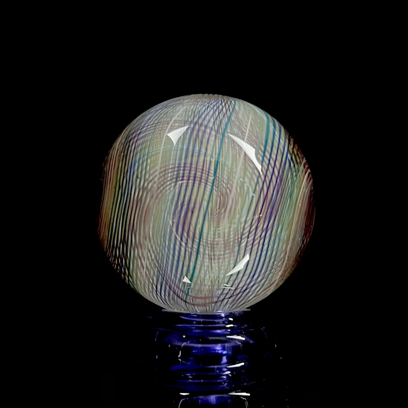 A multicolored glass marble with a mix of vibrant and muted tones, featuring a patterned design. The marble appears to have a convex surface.