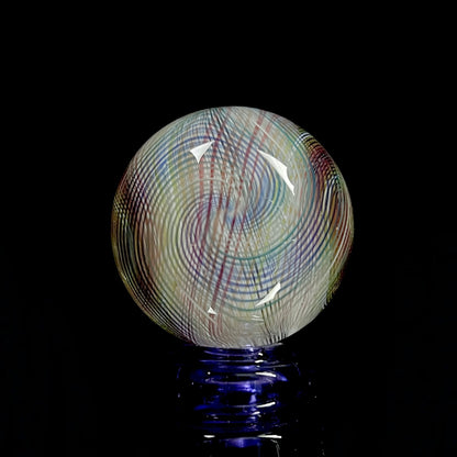 A multicolored glass marble with a mix of vibrant and muted tones, featuring a patterned design. The marble appears to have a convex surface.