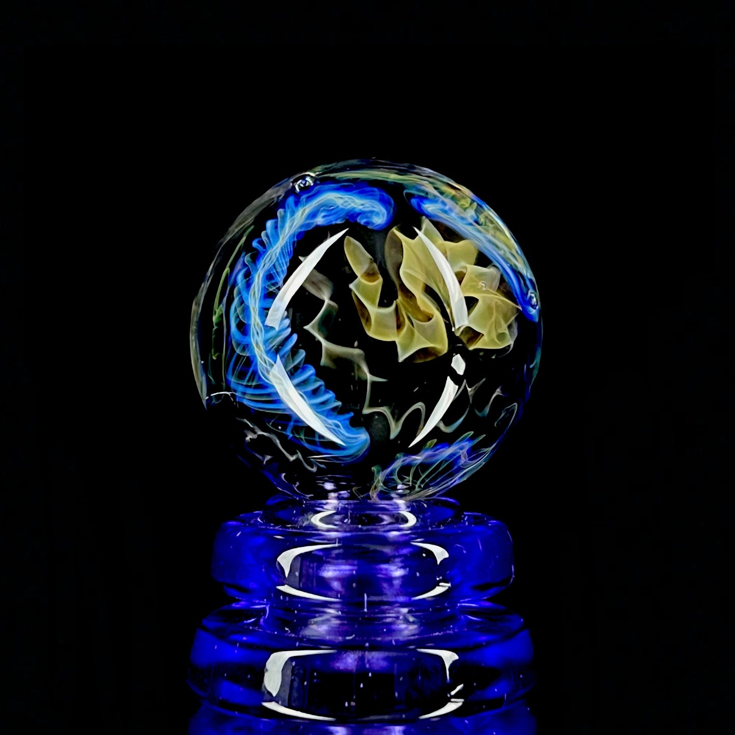 A colorful glass marble with a design featuring blue and yellow, crafted by Phase Glass.