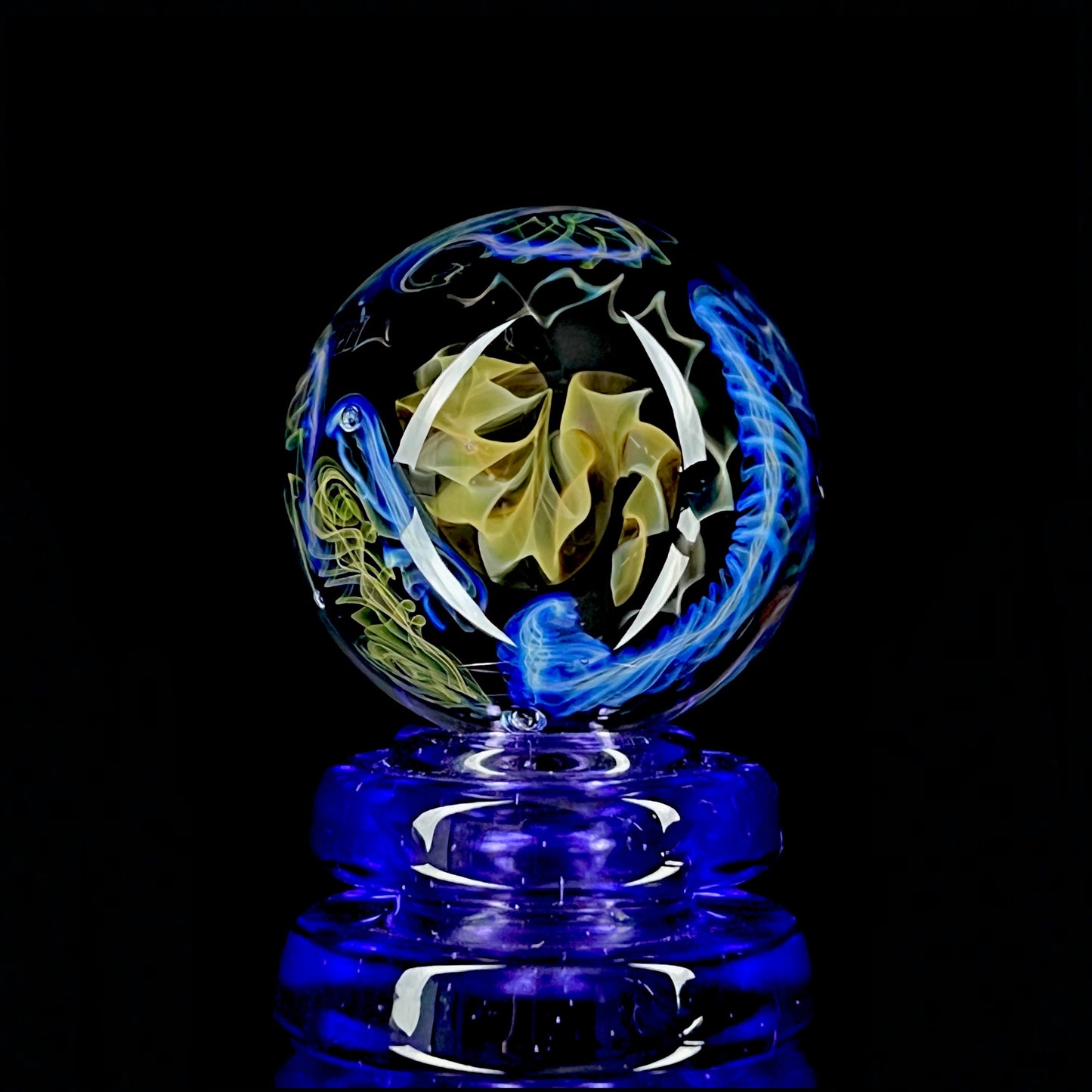 A colorful glass marble with a design featuring blue and yellow, crafted by Phase Glass.