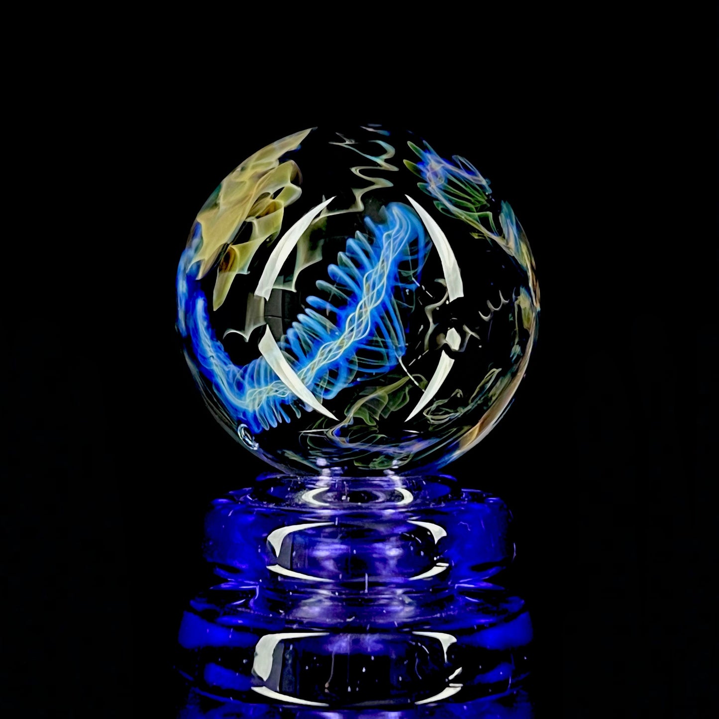 A colorful glass marble with a design featuring blue and yellow, crafted by Phase Glass.