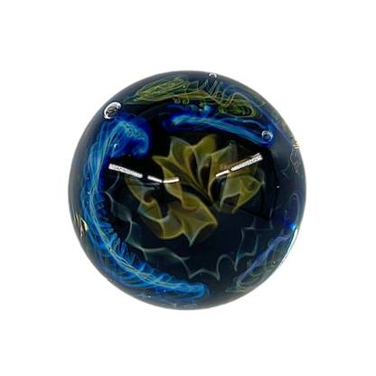 A glass marble with a predominantly blue color and green accents, featuring intricate patterns.