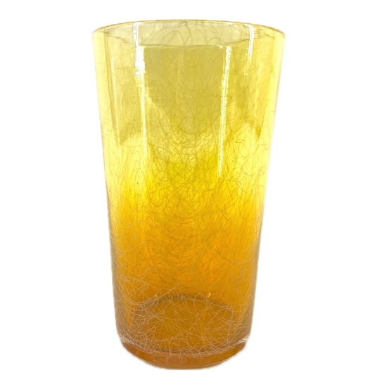 A cylindrical handcrafted glass with yellow and orange hues.