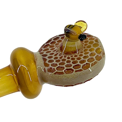 Glass pipe with honeycomb design and bee figure on a white background.