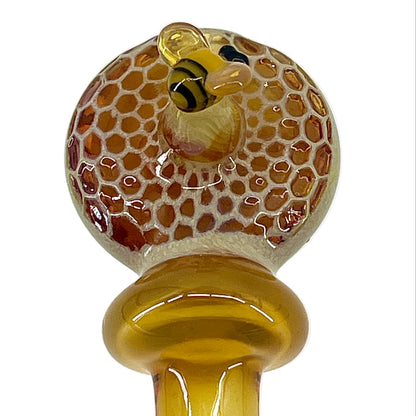 Glass pipe with honeycomb design and bee figure on a white background.