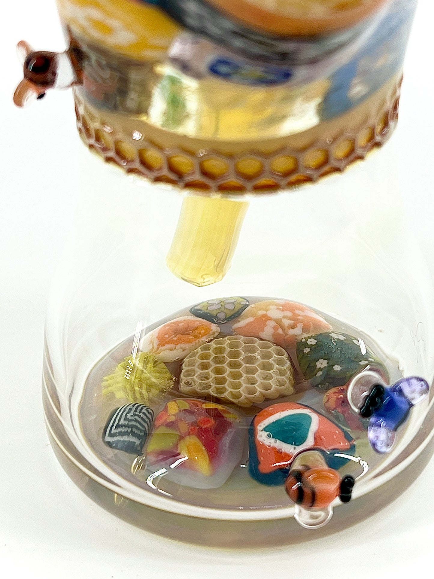 Glass sculpture with colorful millefiori, a bee, and a honeycomb on a white background.