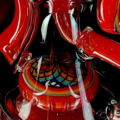 Red and clear glass smoking device with colorful designs on a white background.