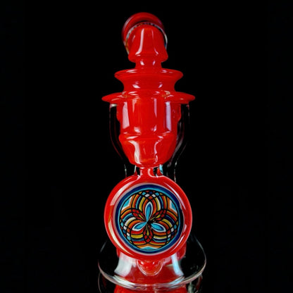 Red and clear glass smoking device with colorful designs on a white background.