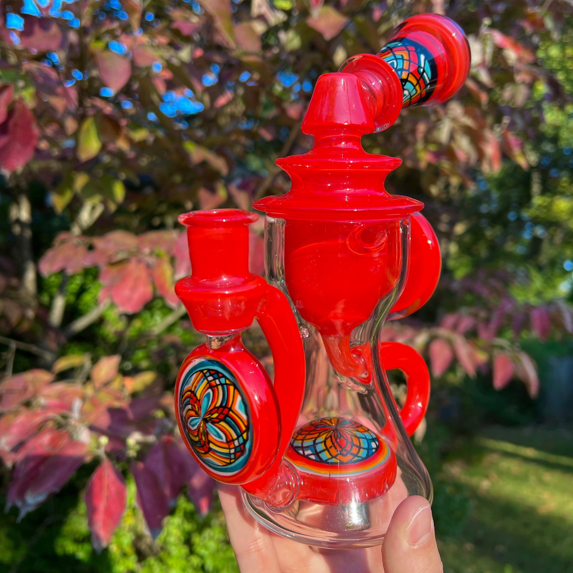 Red and clear glass smoking device with colorful designs on a white background.