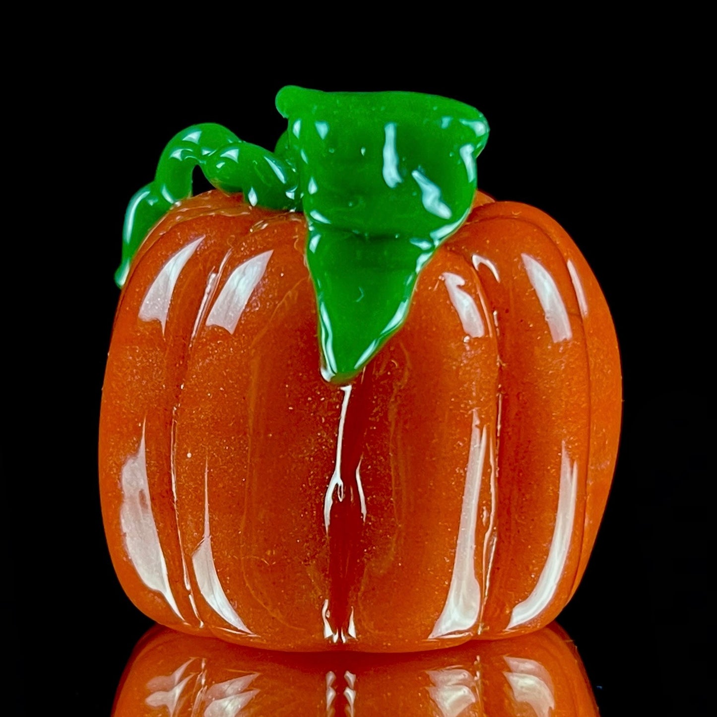 A glass pendant necklace with a orange and green pumpkin-shaped figure on a yellow cord.