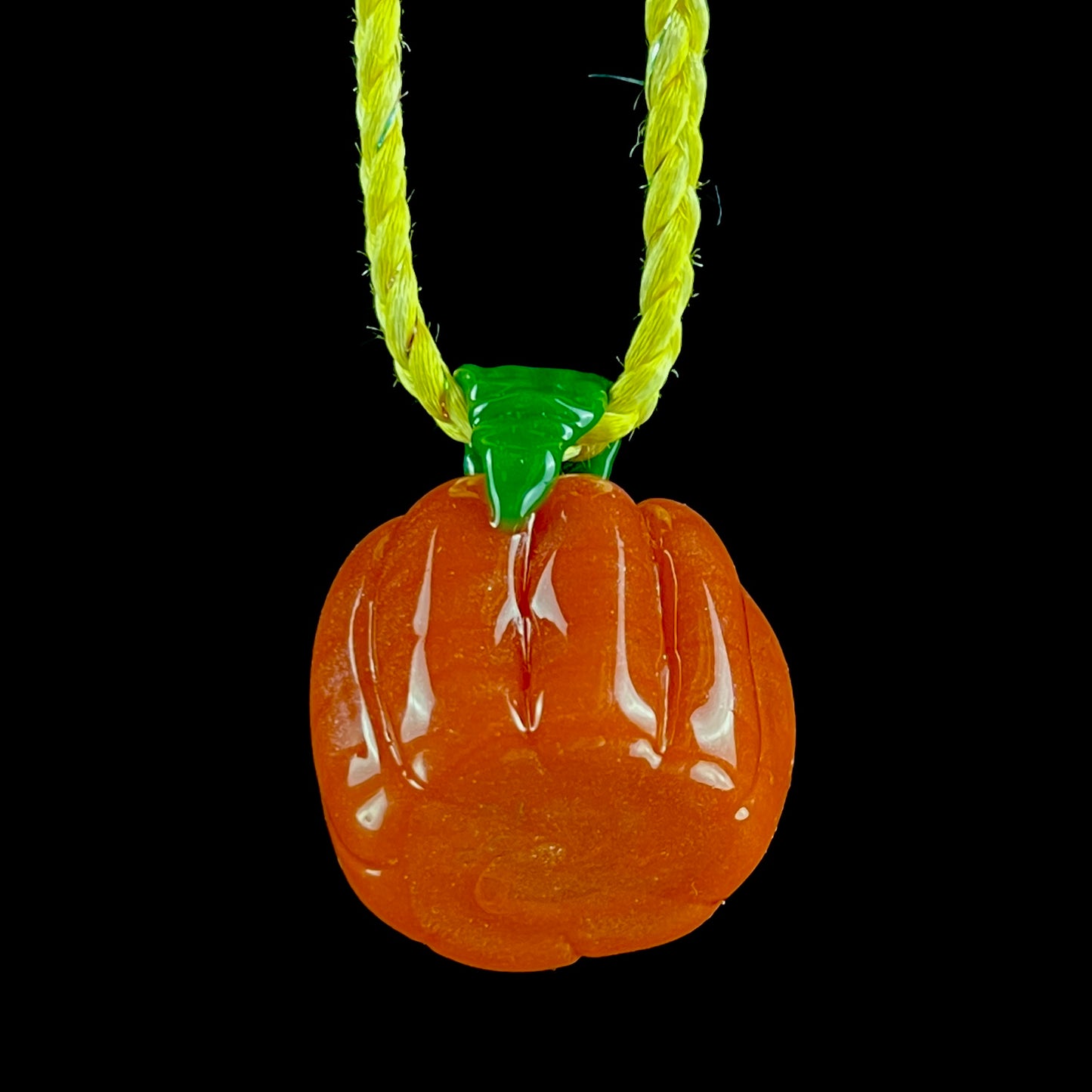A glass pendant necklace with a orange and green pumpkin-shaped figure on a yellow cord.