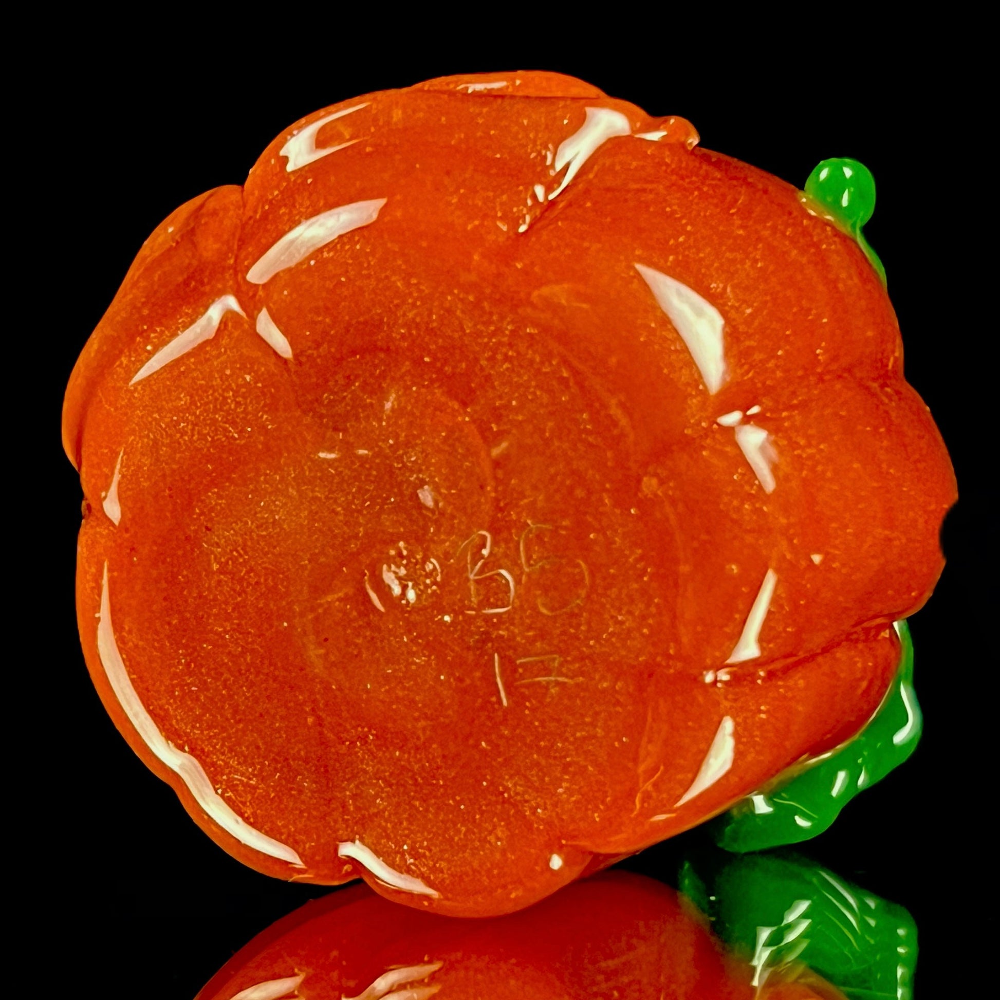 A glass pendant necklace with a orange and green pumpkin-shaped figure on a yellow cord.