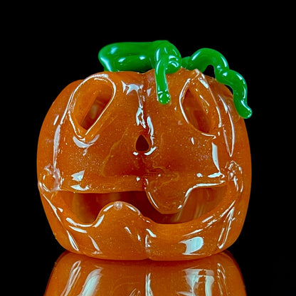 A glass pendant necklace with a orange and green pumpkin-shaped figure on a yellow cord.