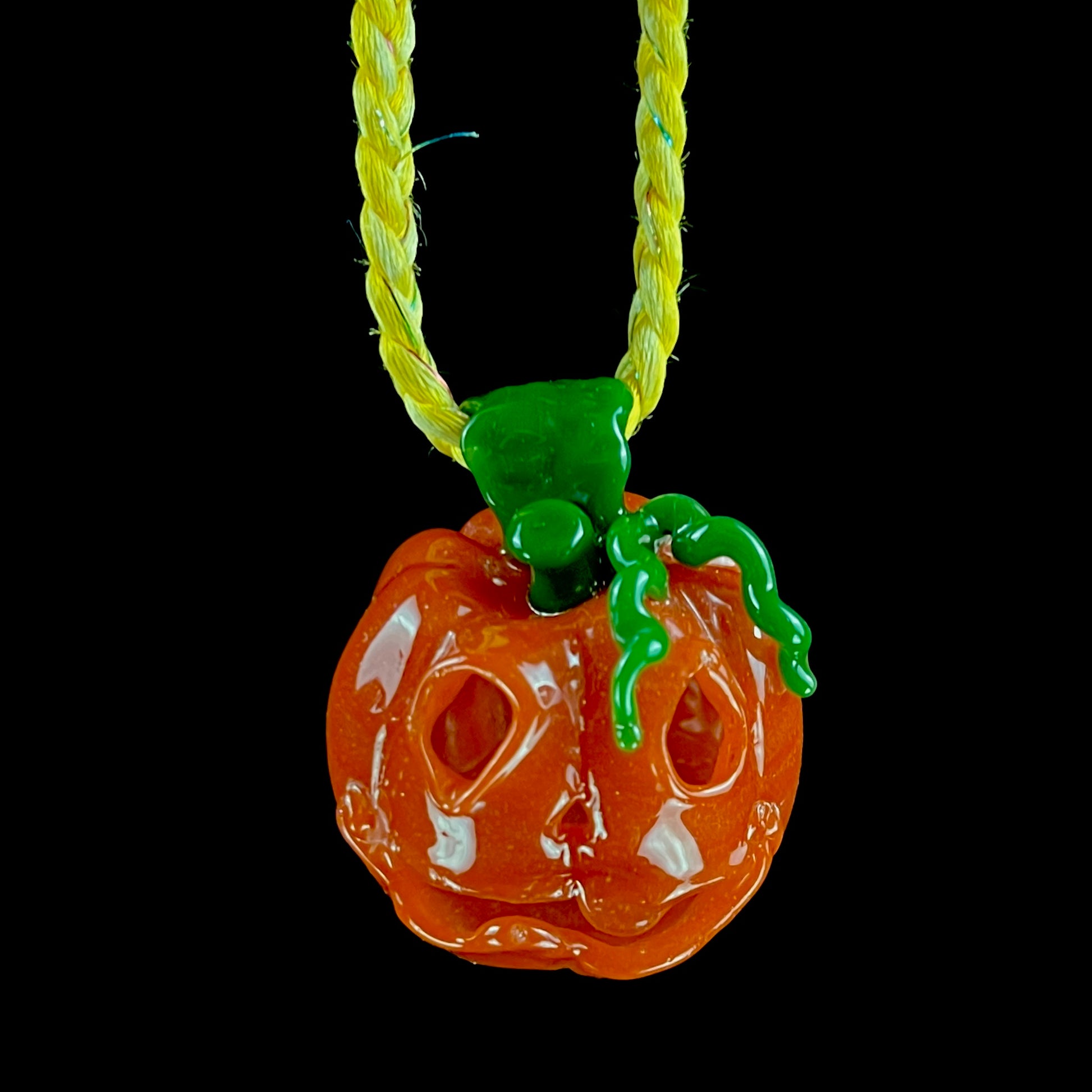A glass pendant necklace with a orange and green pumpkin-shaped figure on a yellow cord.