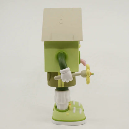 A toy figure of a character resembling a house with eyes, wearing green shorts, a green and white shirt, and green and white shoes, holding a yellow flower.