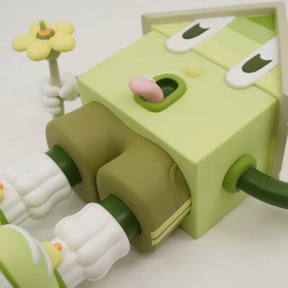 A toy figure of a character resembling a house with eyes, wearing green shorts, a green and white shirt, and green and white shoes, holding a yellow flower.