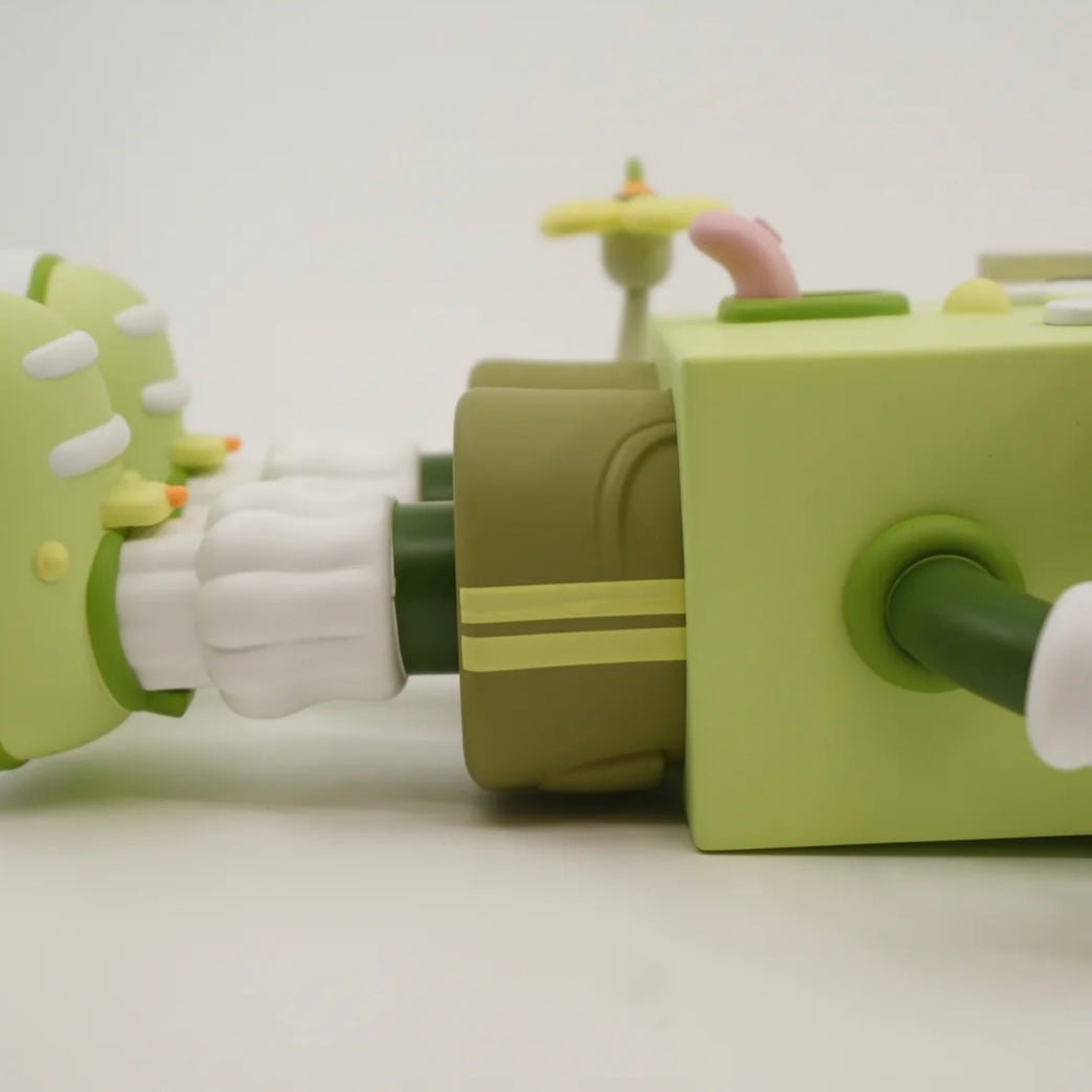 A toy figure of a character resembling a house with eyes, wearing green shorts, a green and white shirt, and green and white shoes, holding a yellow flower.