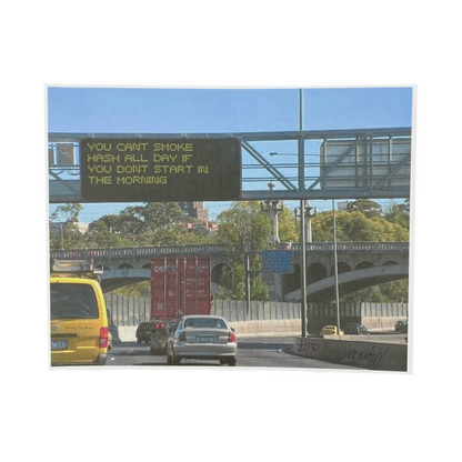 A framed print titled 'Morning Rush' featuring a photograph of a city street scene with a sign above the road, and vehicles and foliage in the background.