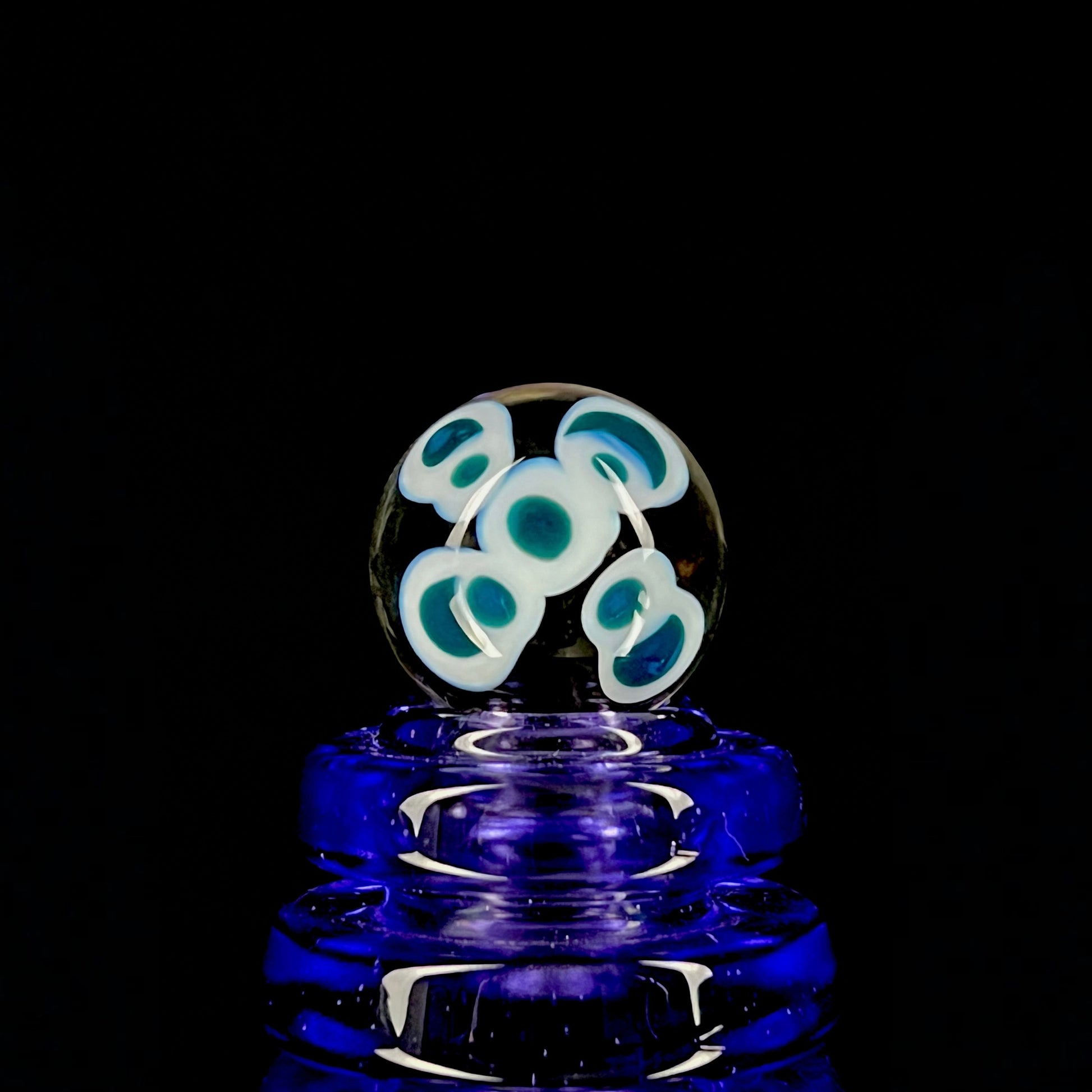 A multicolored glass marble with a design resembling a flower with blue petals on a white background, with a diameter approximately of 22mm.