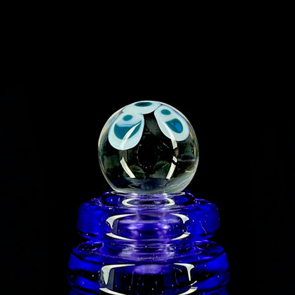 A multicolored glass marble with a design resembling a flower with blue petals on a white background, with a diameter approximately of 22mm.